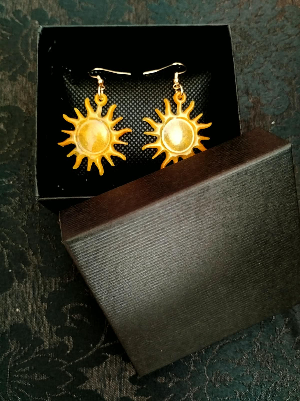 Boucles d'oreille soleil posées sur leur écrin ouvert