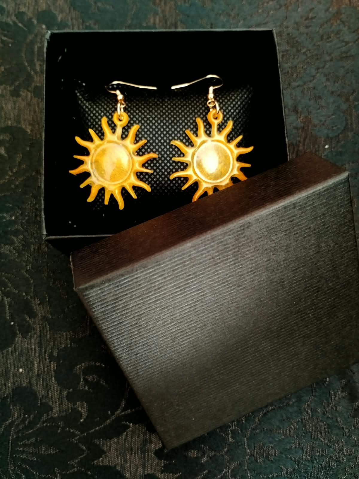 Boucles d'oreille soleil posées sur leur écrin ouvert
